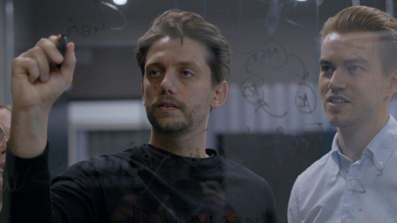 Divi kolēģi raksta idejas uz stikla tāfeles.