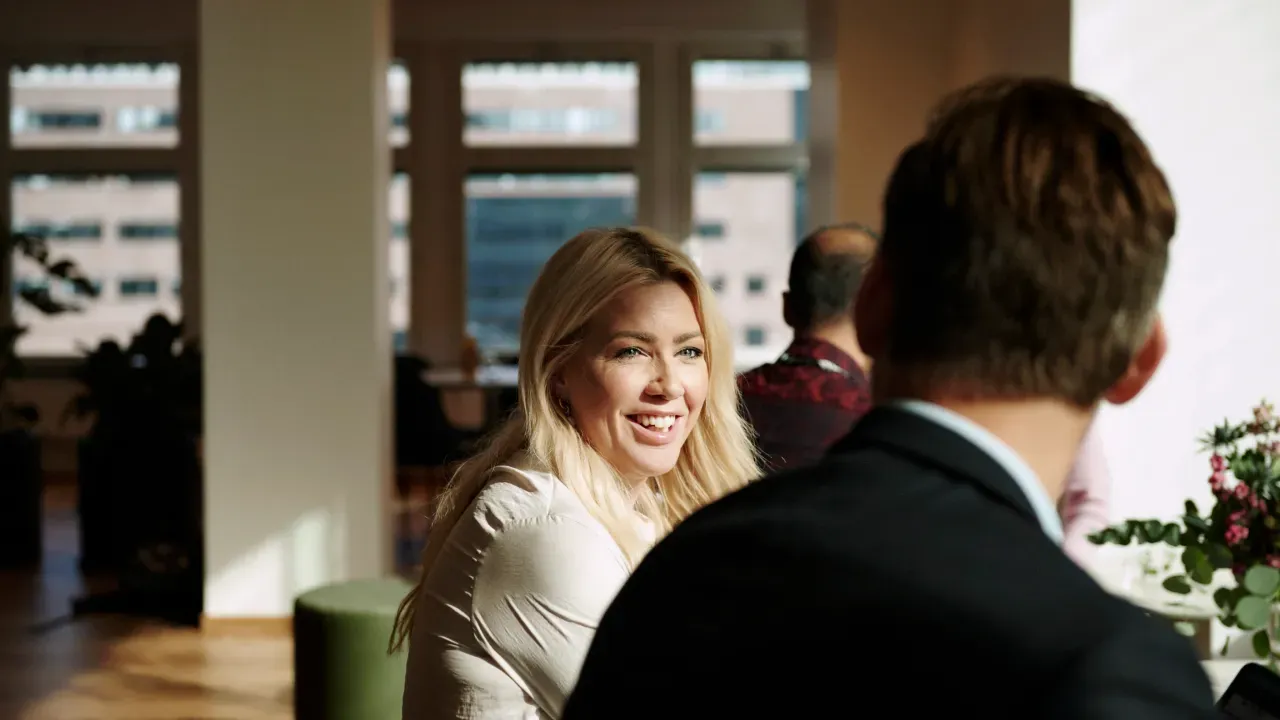 Sieviete smaida sarunā ar kolēģi birojā.