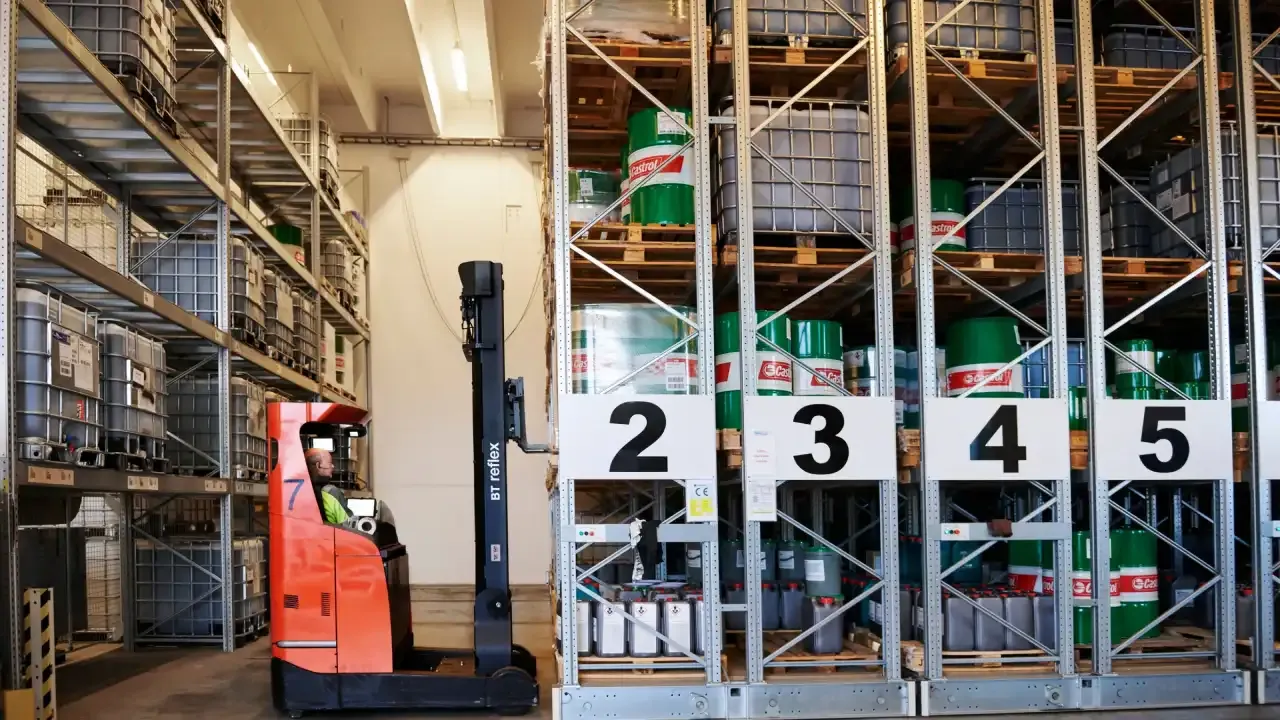 Noliktavas darbinieks ar iekrāvēju pie plauktiem ar konteineriem.