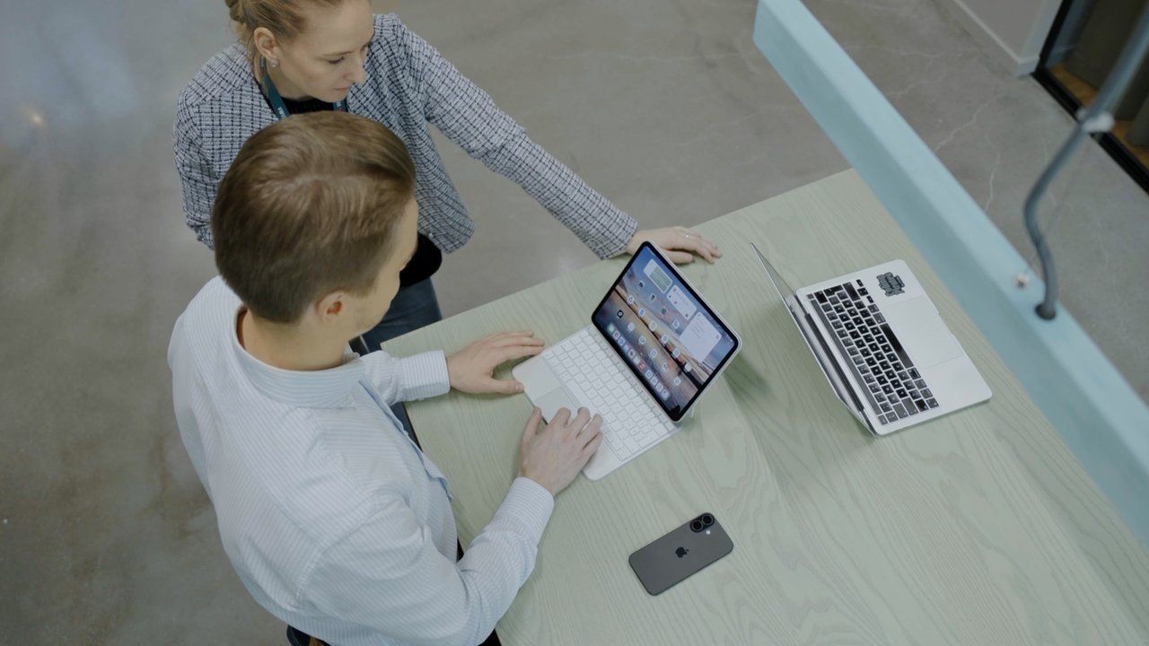 Divi kolēģi strādā pie planšetes un klēpjdatora.