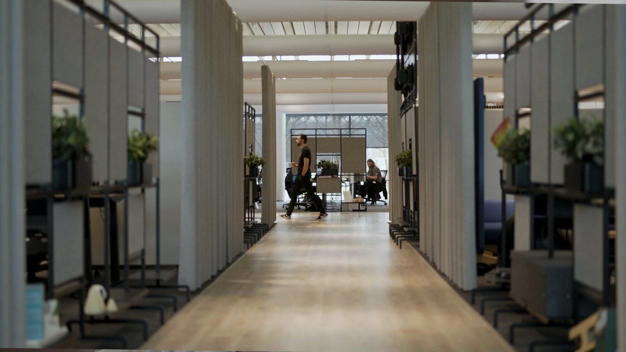 Atvērta tipa biroja telpa ar darba vietām un cilvēkiem.