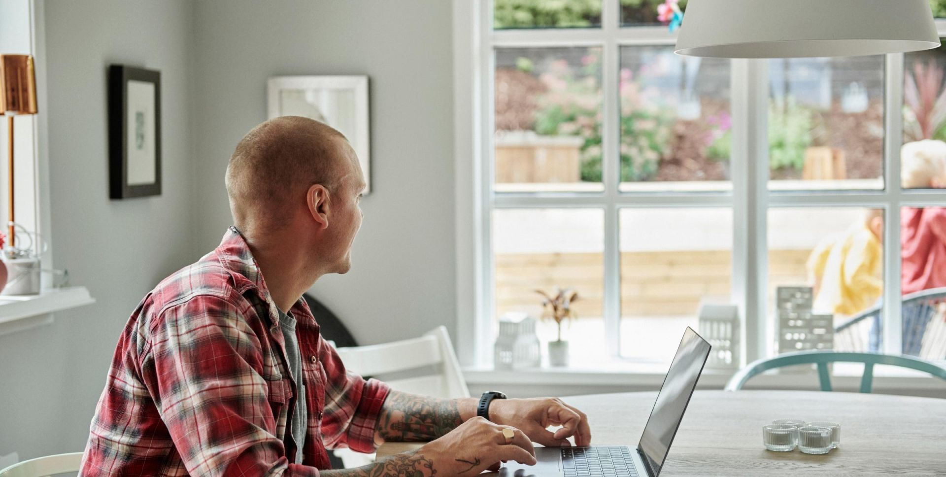 Vīrietis pie klēpjdatora skatās pa logu.