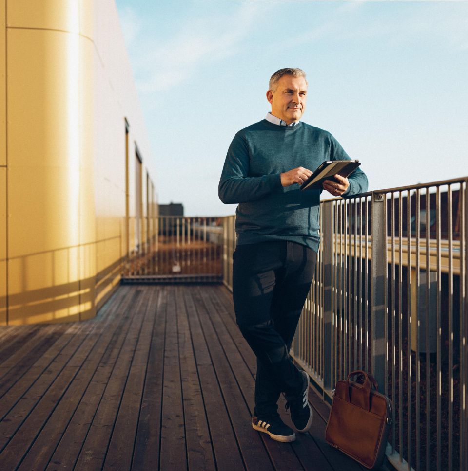 Vīrietis ar planšeti stāv uz jumta terases pie margām.