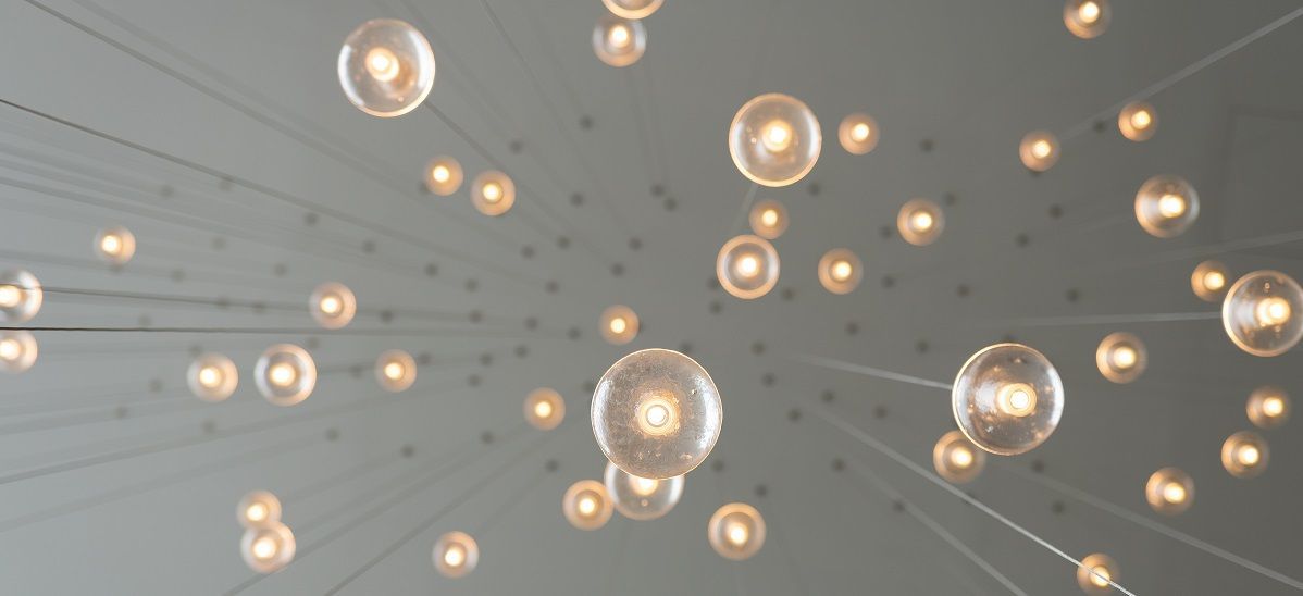 Skats no apakšas uz daudzām degošām, dekoratīvām spuldzītēm, kas karājas vados.