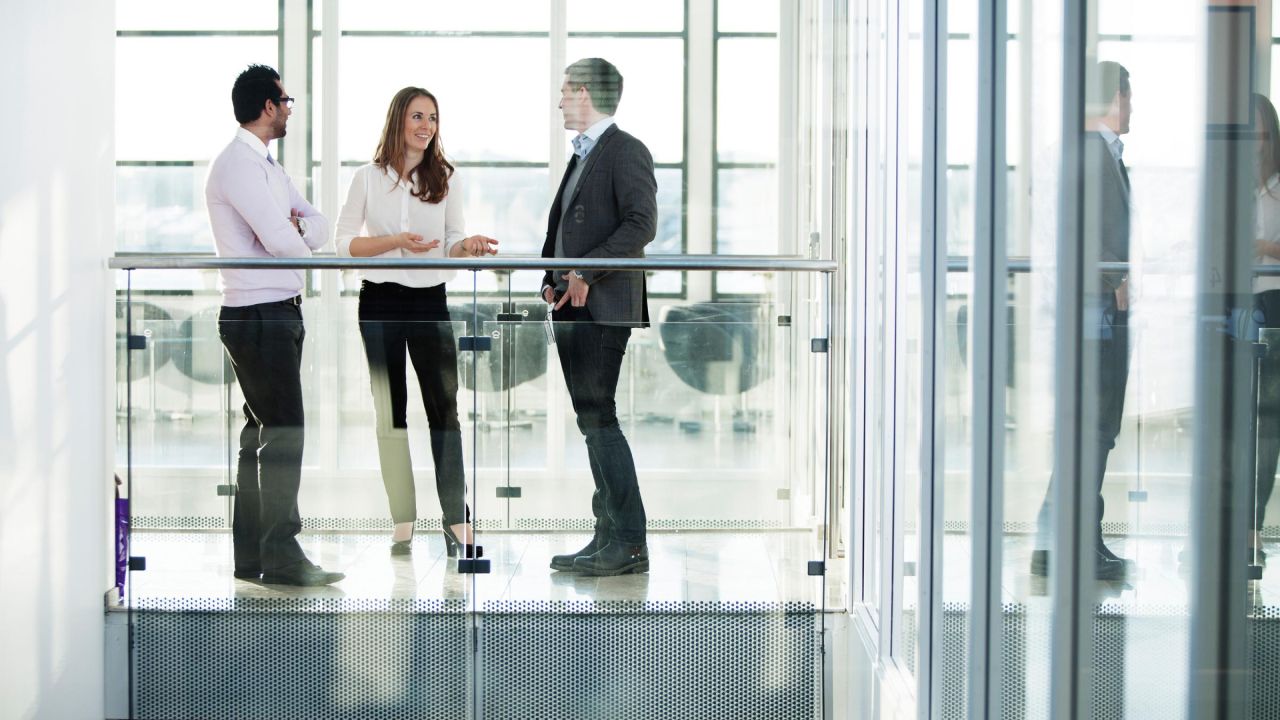 Trīs kolēģi apspriežas gaišā un modernā biroja telpā, veicinot savstarpējo sadarbību.