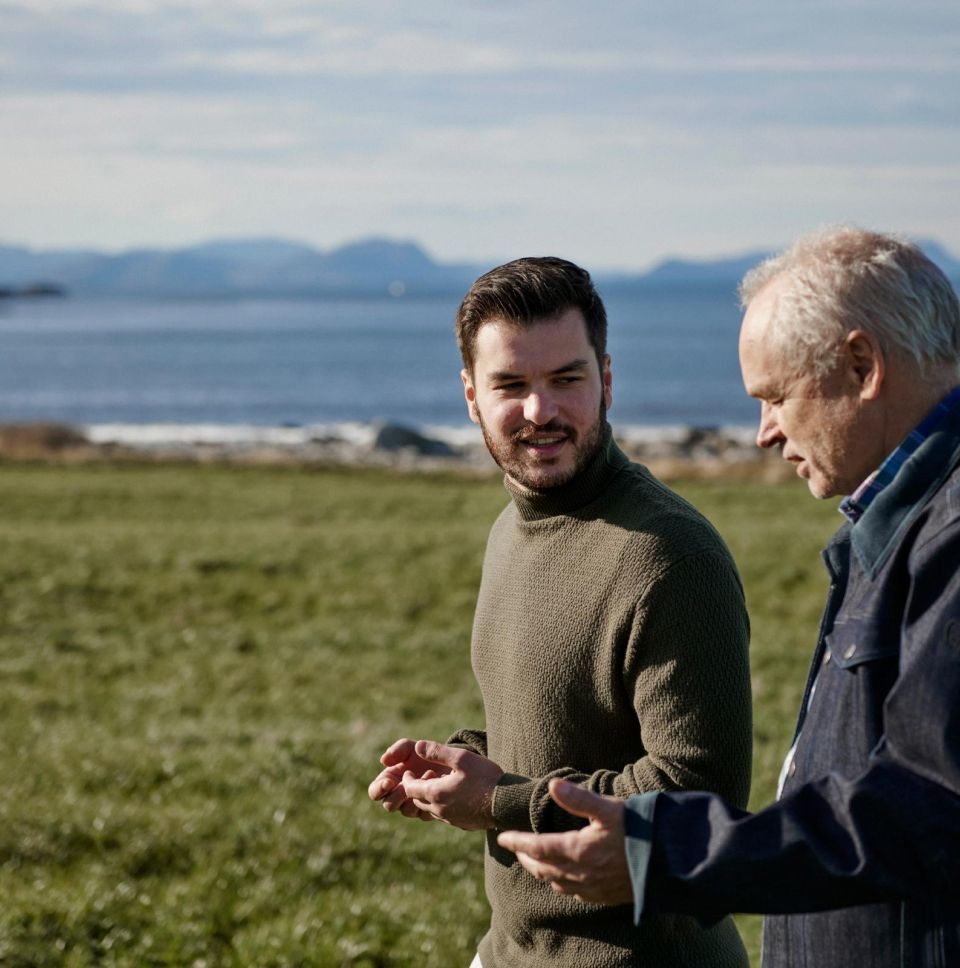 Divi vīrieši sarunājas ārā pie jūras, diskutējot par biznesa jautājumiem.