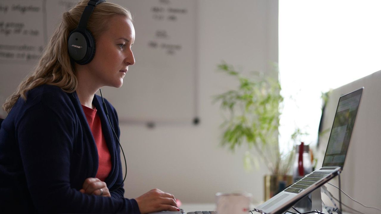 Sieviete ar austiņām koncentrēti strādā pie datora biroja vidē.
